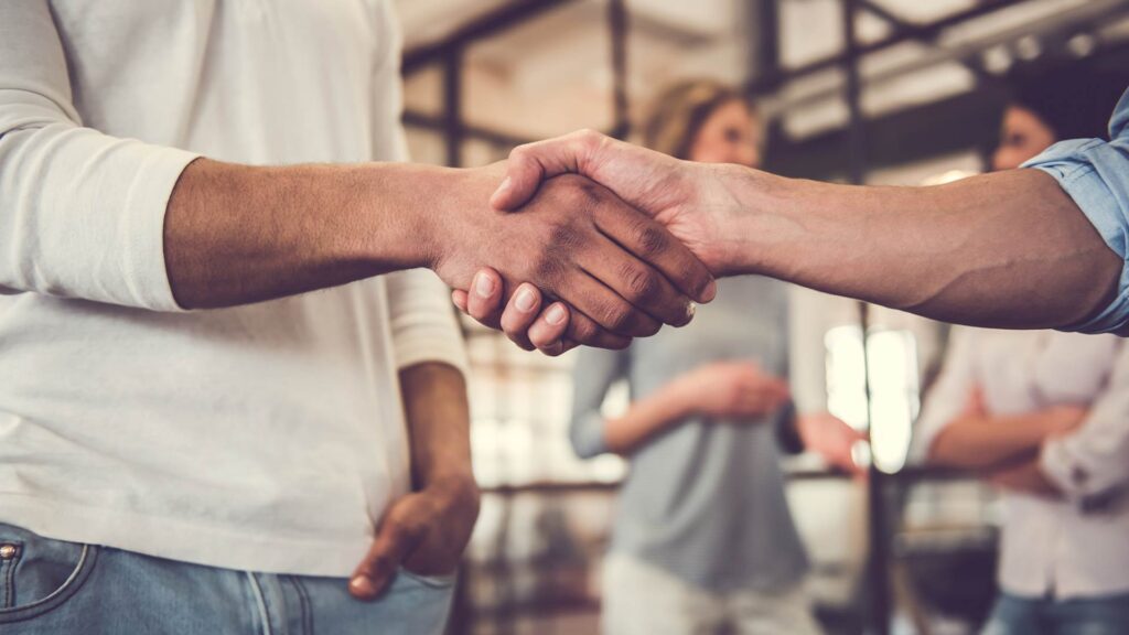 Aperto de mãos entre dois profissionais, simbolizando parceria e confiança promovidas por uma fintech.