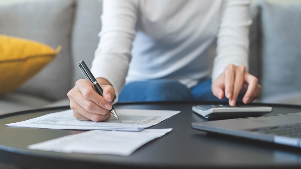 Pessoa preenchendo documentos e utilizando calculadora em atividade relacionada à declaração de imposto de renda.