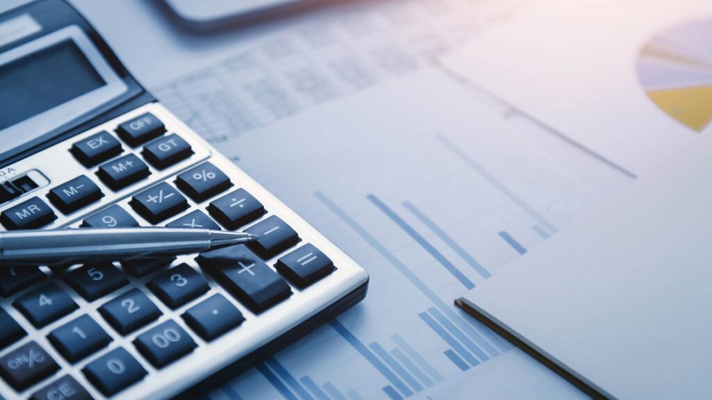 Calculadora e gráficos financeiros sobre mesa, simbolizando o cálculo envolvido na antecipação de recebíveis.