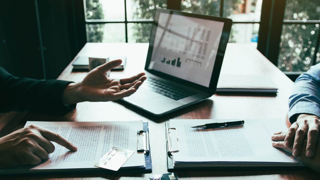 Duas pessoas negociam linhas de crédito com documentos e gráficos financeiros sobre a mesa.