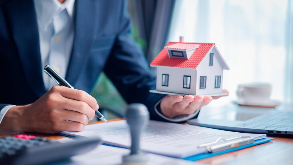 Homem de terno assinando contrato enquanto segura uma maquete de casa, representando contratação de crédito via home equity.