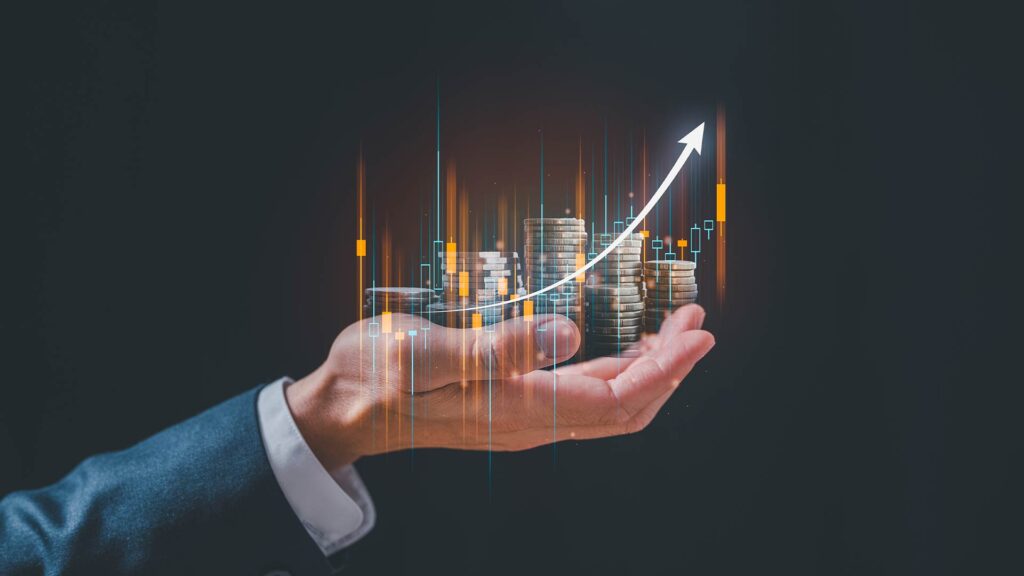 Mão segurando moedas com gráficos e seta de crescimento, representando o crescimento dos investimentos em produtos financeiros.