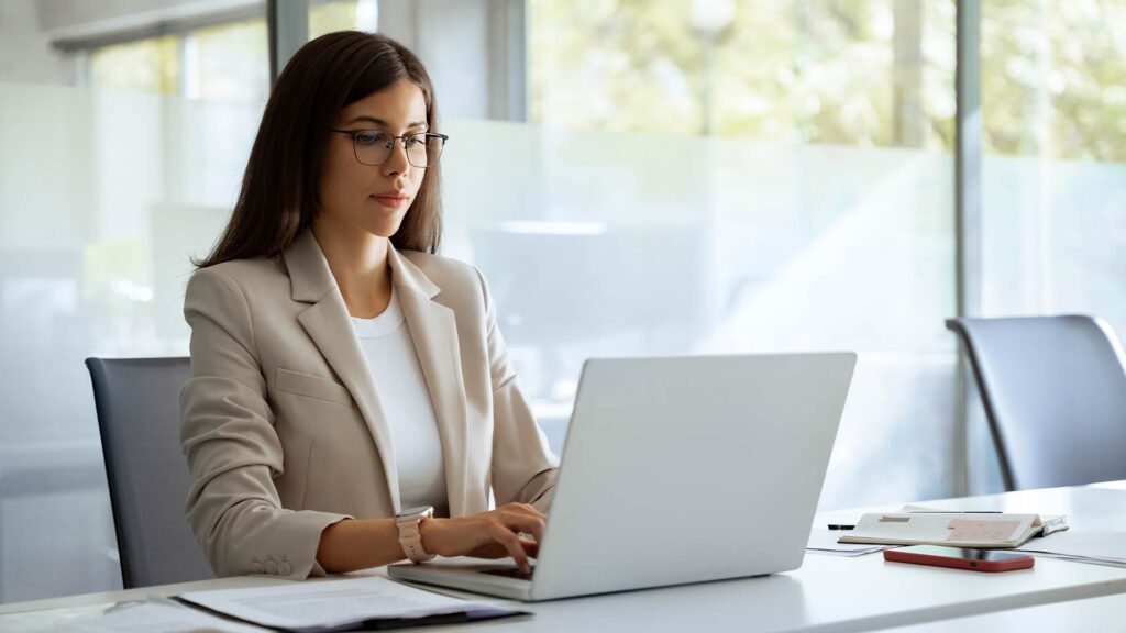 Mulher digitando em notebook em escritório moderno, representando um bancário autônomo de sucesso.