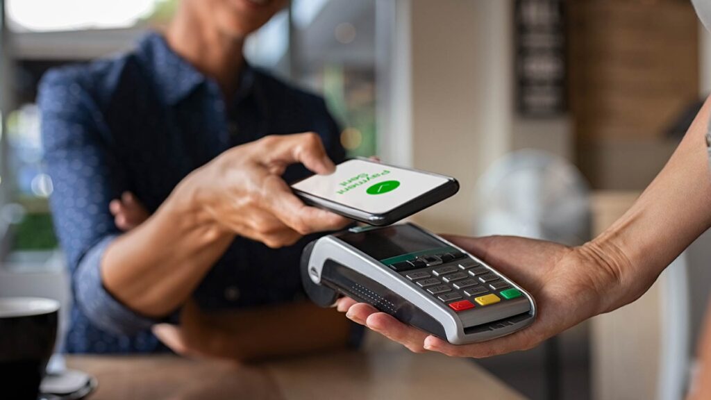 Cliente realizando pagamento por aproximação com celular, ilustrando mudanças no comportamento do consumidor e a preferência por soluções financeiras digitais.