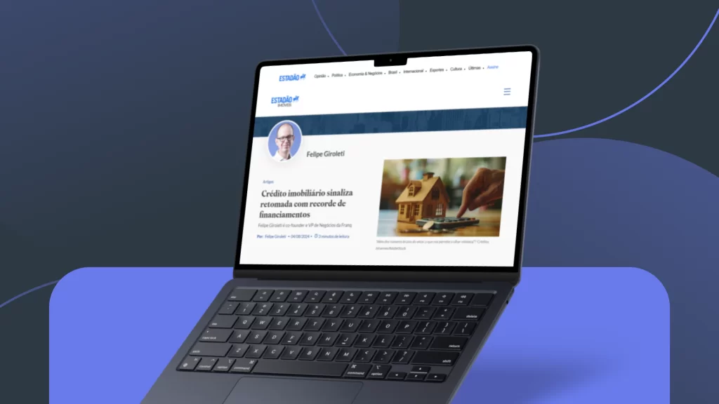 Laptop exibindo um artigo do Estadão escrito por Felipe Giroleti sobre a retomada do crédito imobiliário e o recorde de financiamentos. A tela mostra uma foto de uma miniatura de casa ao lado de uma calculadora, reforçando o tema financeiro