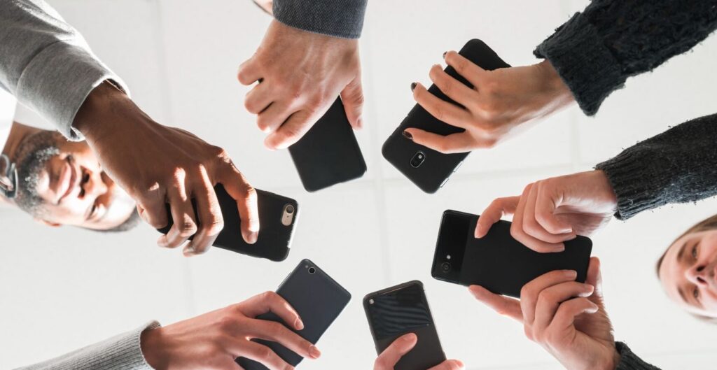 Grupo de pessoas em círculo segurando smartphones voltados para o centro, vistos de um ângulo inferior. Conceito de união digital e Multi-Banking.
