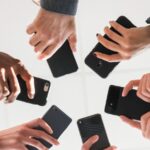 Grupo de pessoas em círculo segurando smartphones voltados para o centro, vistos de um ângulo inferior. Conceito de união digital e Multi-Banking.