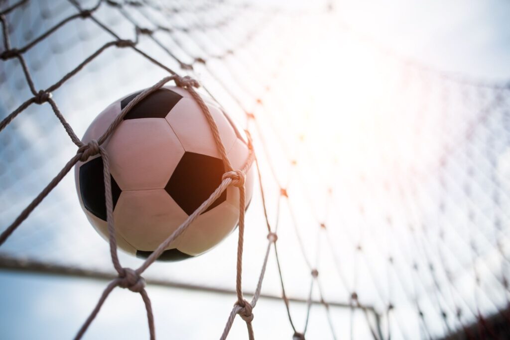 Bola de futebol entrando no gol e batendo na rede.