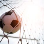 Bola de futebol entrando no gol e batendo na rede.