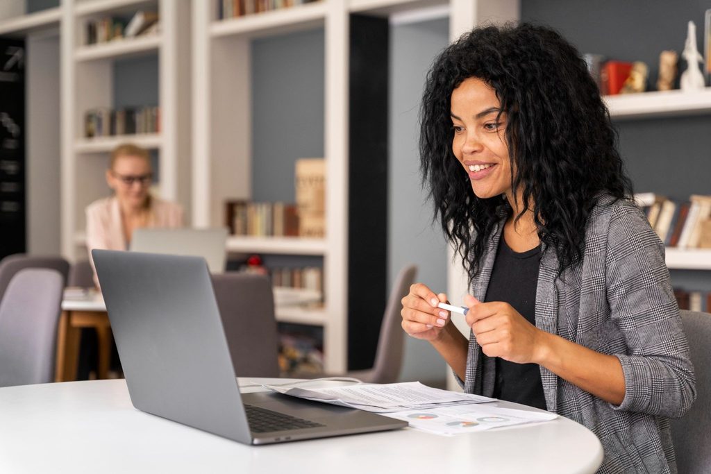 Mulher sorridente à frente de um portátil num escritório, a analisar documentos. Imagem a representar a consultoria do Personal Banker na escolha entre empréstimo e financiamento.