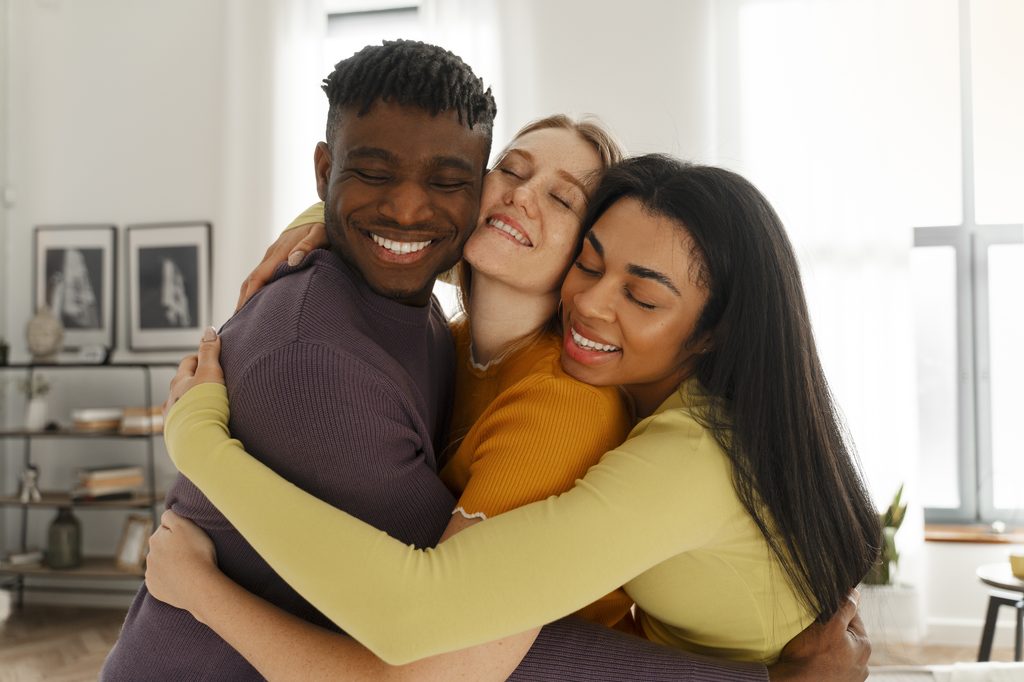 Grupo de três amigos sorrindo e se abraçando afetuosamente, ilustrando que seguro de vida não é tudo igual e varia conforme cada momento.