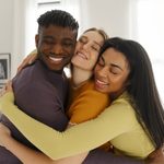 Grupo de três amigos sorrindo e se abraçando afetuosamente, ilustrando que seguro de vida não é tudo igual e varia conforme cada momento.